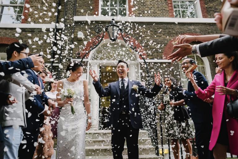 Couple leaving wedding venue under confetti